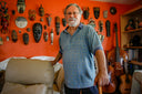 Man standing in a warm orange colored room with musical instruments and ornate tribal mask wall decorations.